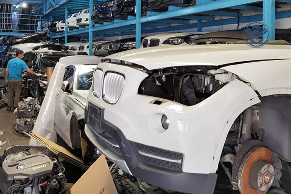 واجهة BMW بيضاء مفككة دون المصباح الأمامي مع قرص فرامل ظاهر وقطع محيطة داخل مستودع