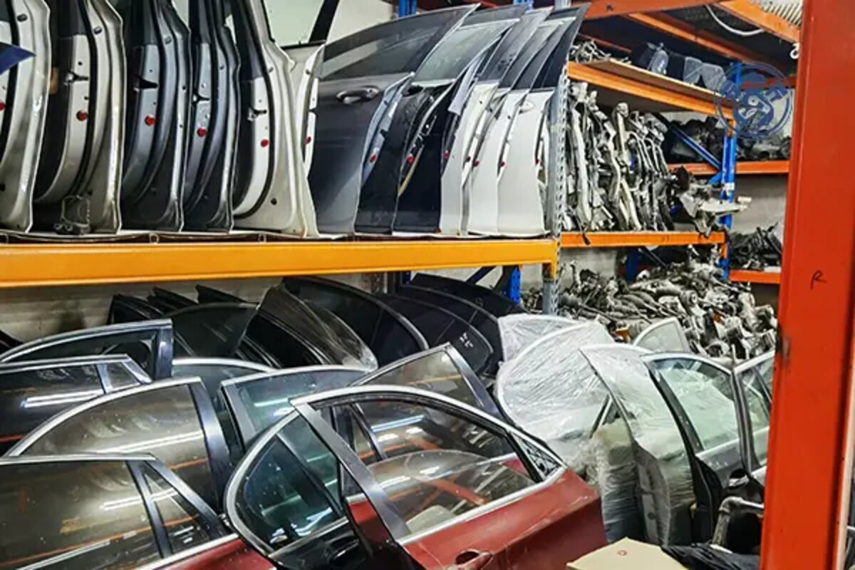 أبواب وقطع هيكل مختلفة على رفوف زرقاء وبرتقالية داخل مستودع